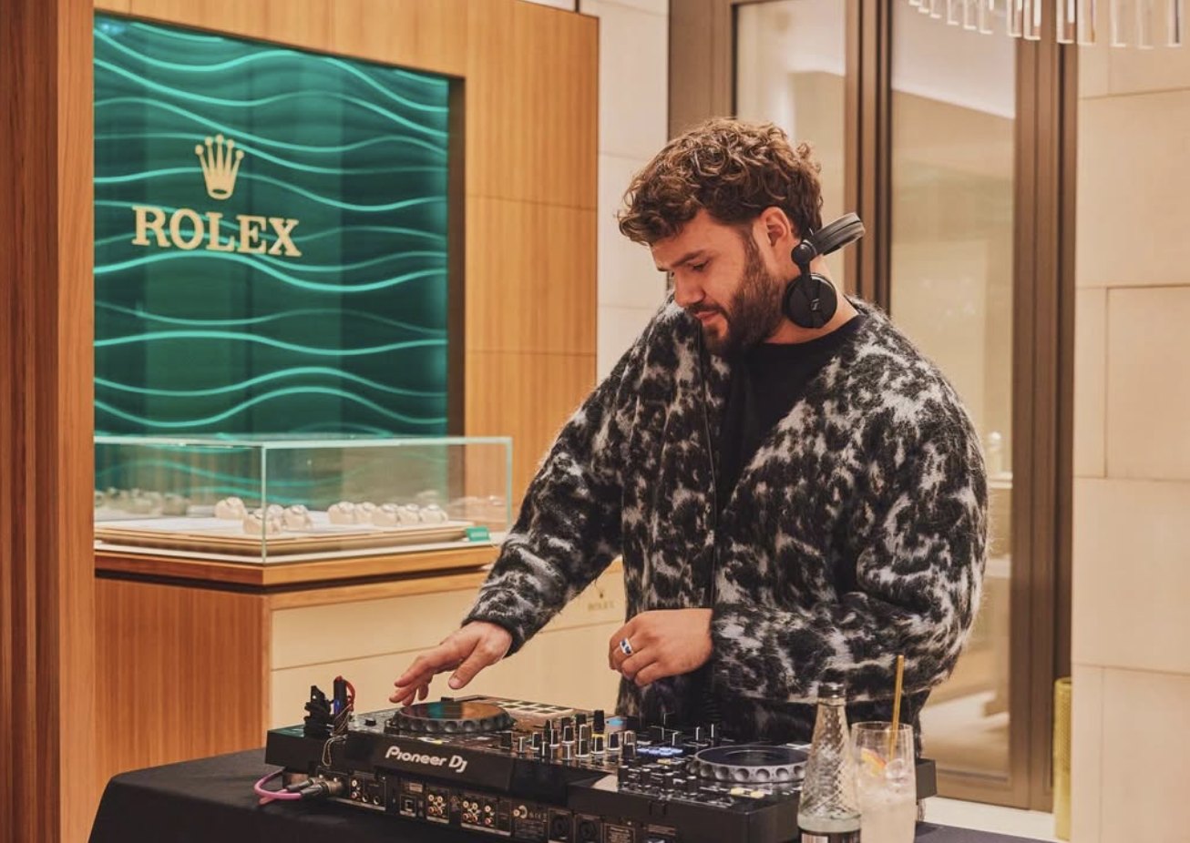 A DJ at the decks beside a Rolex display