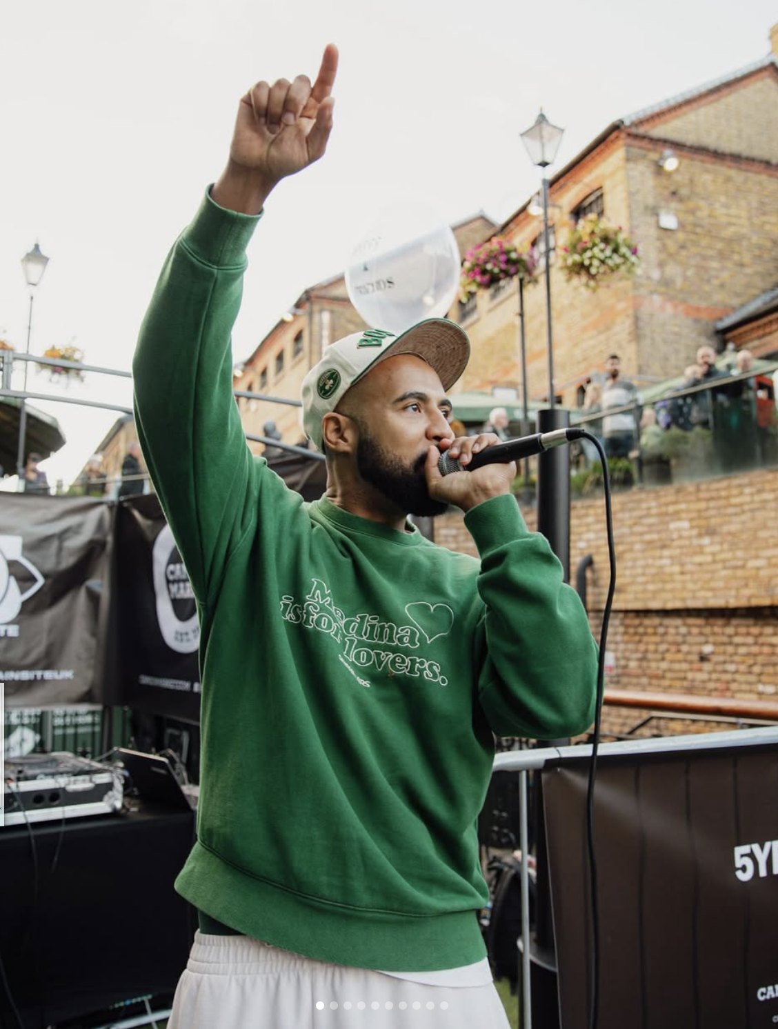 A performer on the mic with one arm raised, outdoors at Camden Market