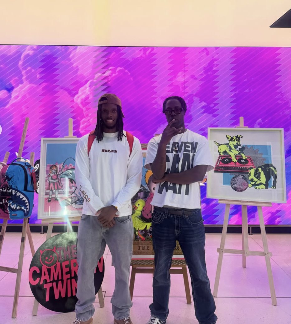 Two guests standing among framed artworks on easels in front of a purple screen